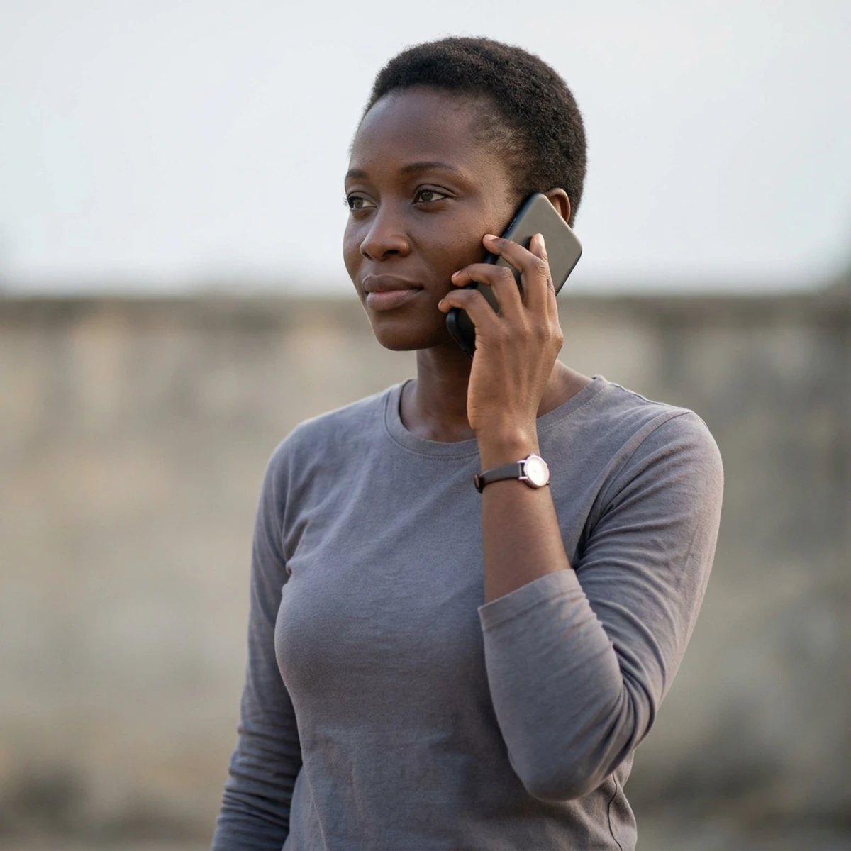 A woman holds a phone to her ear outdoors in a listening posture