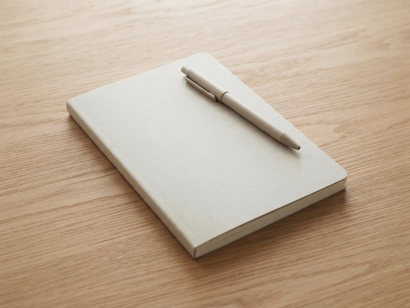 Single plain notebook with a pen resting on top of it on a wooden desk