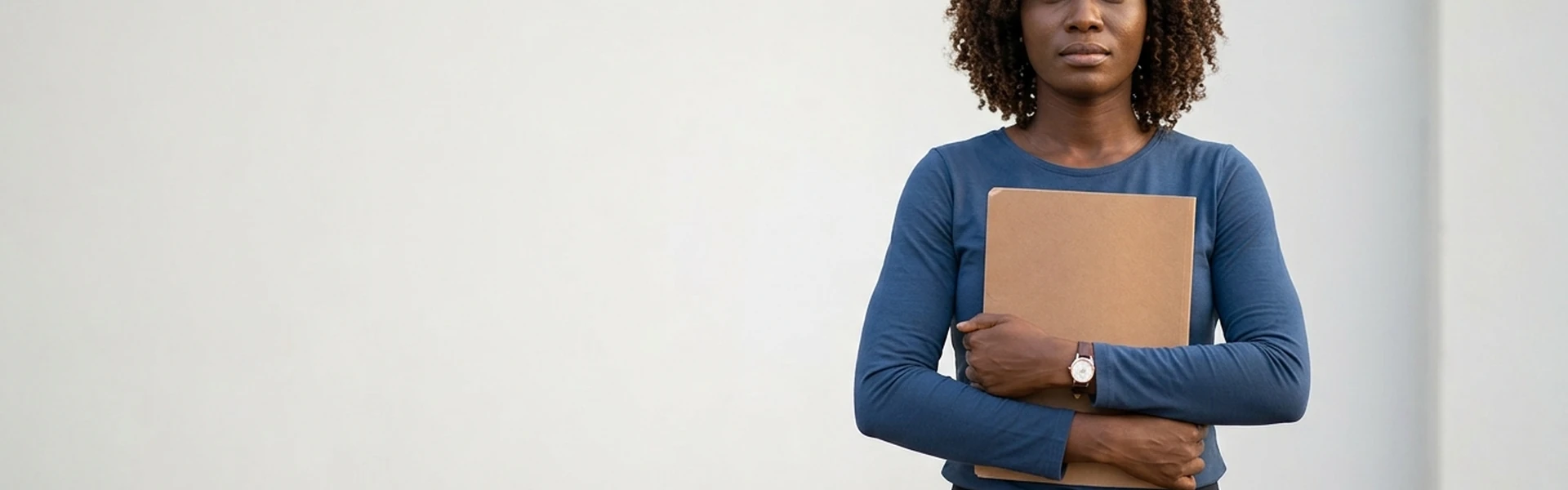 A Nigerian woman holds a plain closed folder against her chest with both hands