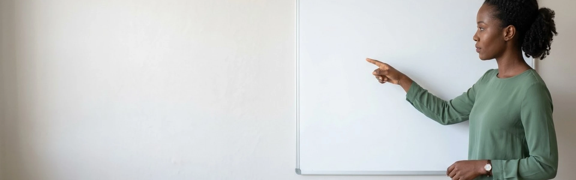 A Nigerian woman stands beside a whiteboard and points at it with one hand